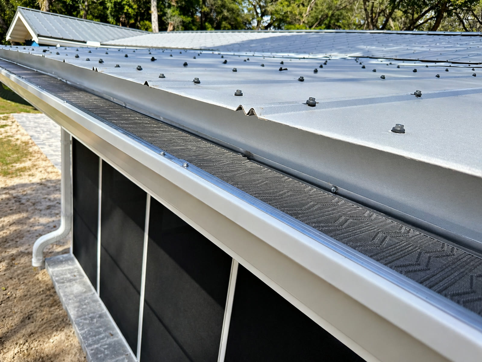 Close-up of a standing seam metal roof panel overhanging a white seamless gutter with micro-mesh leaf protection, installed by Gutters C2U.